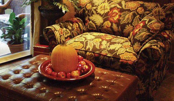 A pumpkin and group of apples resting on a tray that sits on top of an ottoman.