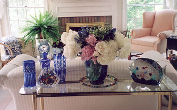 A vase full of flowers with other decorations and a fish tank on top of a glass end table.